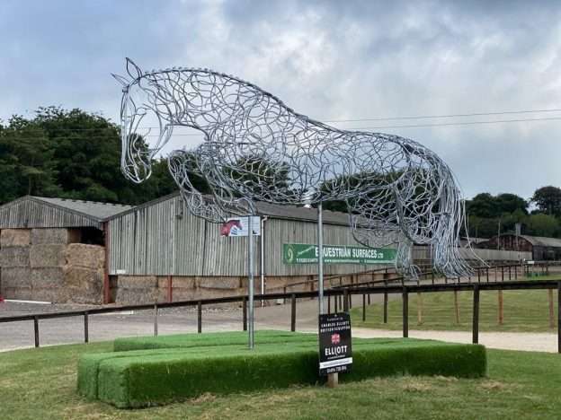 large horse jumping sculpture in front of barns